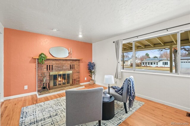 living area featuring a brick fireplace, a textured ceiling, baseboards, and wood finished floors