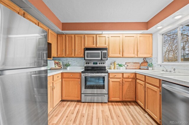 kitchen featuring tasteful backsplash, stainless steel appliances, light countertops, light wood-type flooring, and a sink