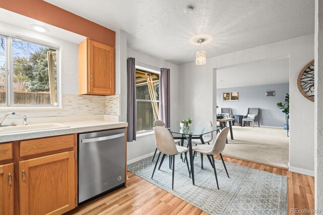 kitchen featuring a sink, light wood-style floors, light countertops, dishwasher, and tasteful backsplash