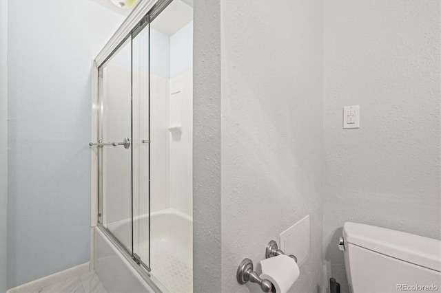 bathroom featuring enclosed tub / shower combo, a textured wall, toilet, and baseboards