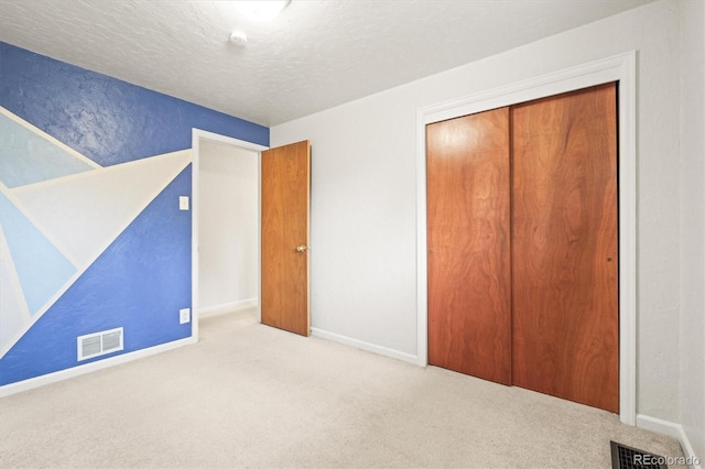 unfurnished bedroom featuring a textured ceiling, a closet, carpet flooring, and visible vents