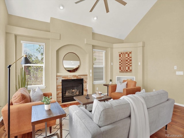 living area featuring a ceiling fan, wood finished floors, a tiled fireplace, baseboards, and high vaulted ceiling
