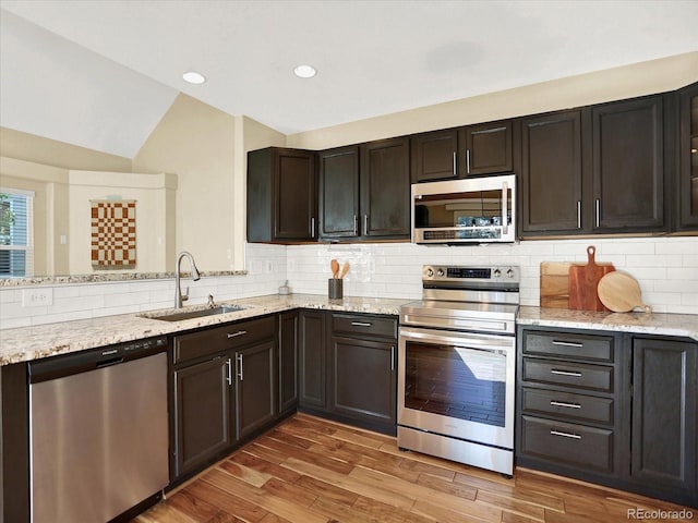 kitchen with stainless steel appliances, a sink, vaulted ceiling, tasteful backsplash, and light stone countertops