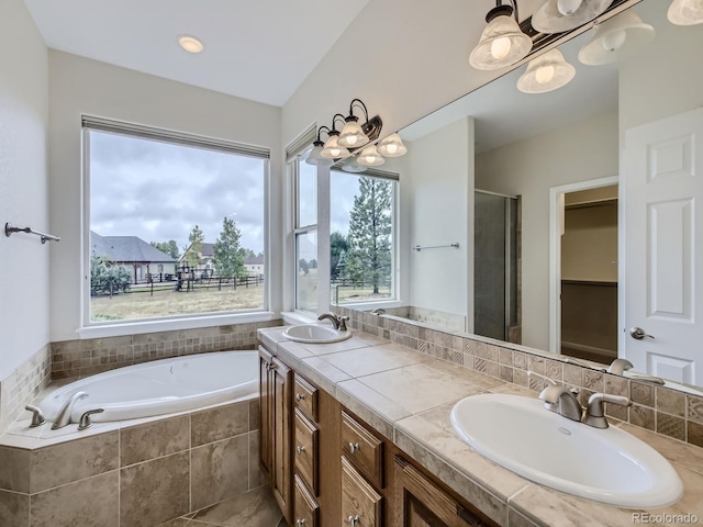 bathroom with a wealth of natural light, double sink vanity, and tiled bath