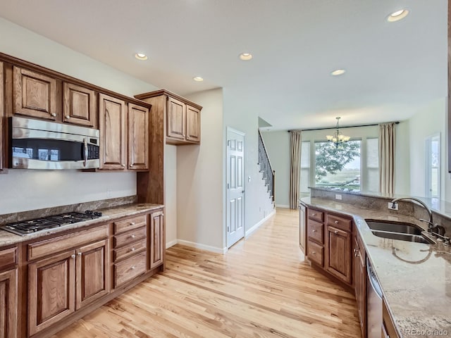 kitchen featuring stainless steel appliances, light hardwood / wood-style floors, light stone counters, a chandelier, and sink