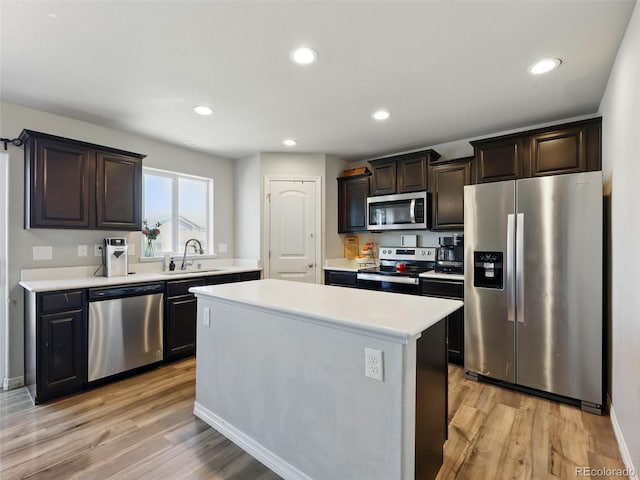 kitchen featuring appliances with stainless steel finishes, a sink, light countertops, light wood finished floors, and dark brown cabinetry
