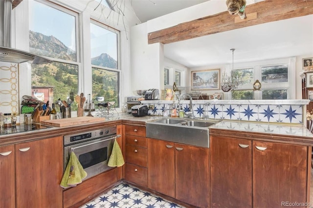 kitchen with oven, wall chimney range hood, lofted ceiling, and a sink