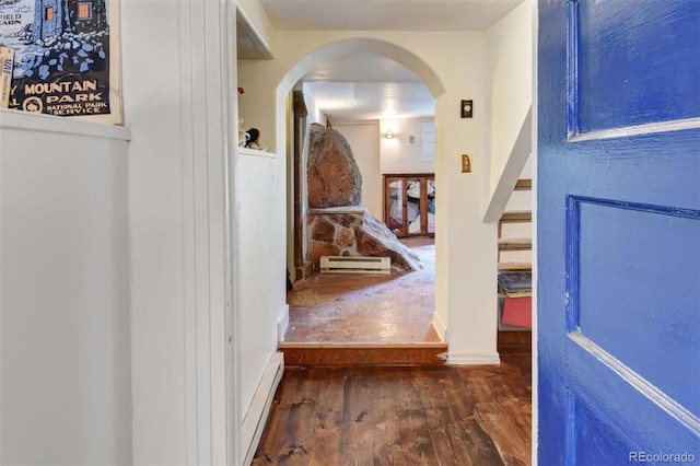 corridor featuring a baseboard heating unit, wood finished floors, and arched walkways