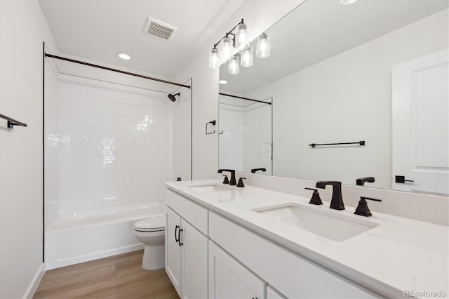 full bathroom with hardwood / wood-style flooring, vanity, tiled shower / bath, and toilet