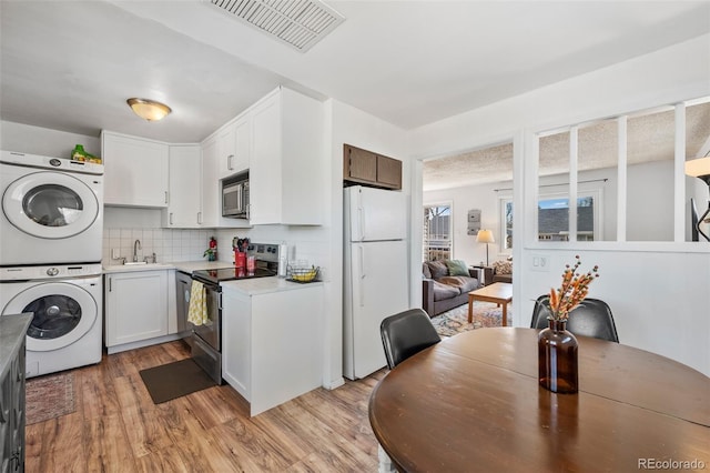 kitchen featuring visible vents, stacked washing maching and dryer, a sink, stainless steel appliances, and light countertops