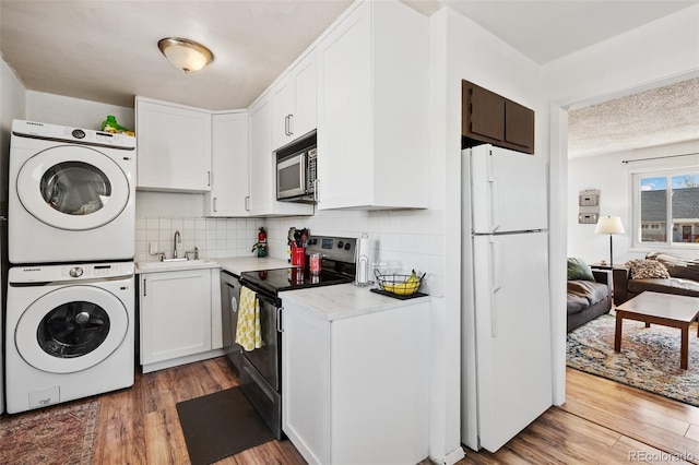 kitchen featuring a sink, freestanding refrigerator, stacked washer / drying machine, light countertops, and stainless steel electric range oven