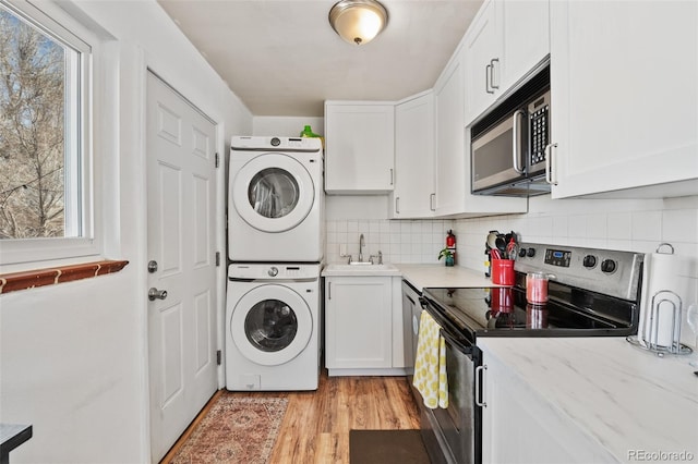 clothes washing area with a healthy amount of sunlight, laundry area, a sink, light wood-style floors, and stacked washer and clothes dryer