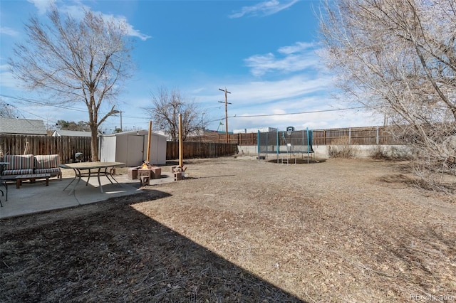 view of yard with a trampoline, a fenced backyard, a shed, and a patio area