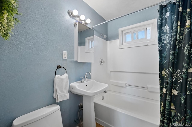 bathroom featuring shower / bath combination with curtain, toilet, and a textured wall