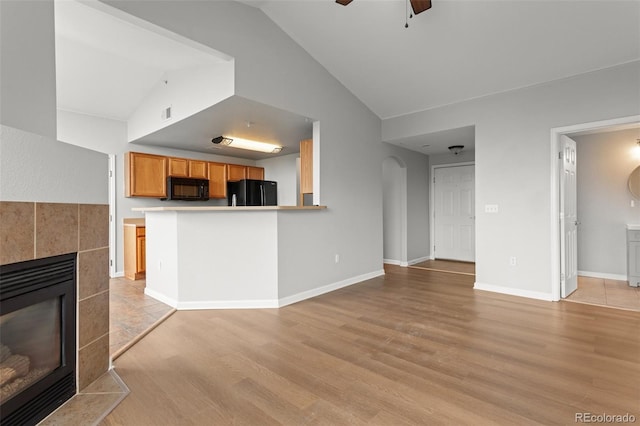 7440 S Blackhawk St Unit 207, Englewood, CO 80112 - unfurnished living room featuring lofted ceiling, a tile fireplace, light wood finished floors, a ceiling fan, and arched walkways