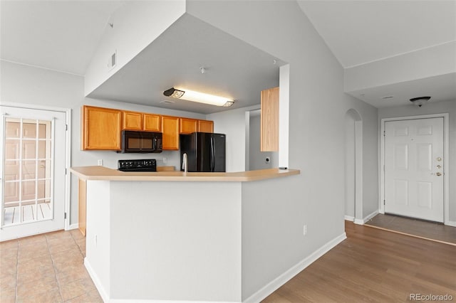 7440 S Blackhawk St Unit 207, Englewood, CO 80112 - kitchen featuring black appliances, arched walkways, light countertops, lofted ceiling, and a peninsula