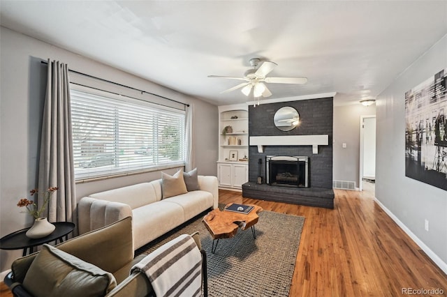 living room with wood finished floors, baseboards, visible vents, a fireplace, and ceiling fan