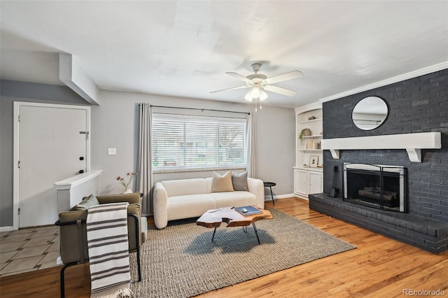 living area featuring built in shelves, a brick fireplace, baseboards, ceiling fan, and wood finished floors