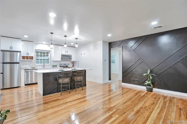 1325 Dayton St, Aurora, CO 80010 - kitchen featuring appliances with stainless steel finishes, white cabinetry, a breakfast bar, light wood-style floors, and light countertops