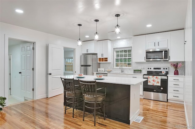 1325 Dayton St, Aurora, CO 80010 - kitchen with stainless steel appliances, light countertops, light wood-type flooring, a center island, and white cabinetry