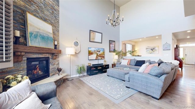 living room featuring wood-type flooring, a towering ceiling, a notable chandelier, and a fireplace