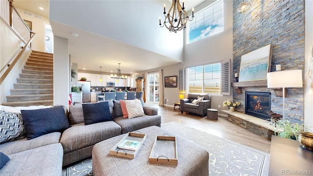 living room with a high ceiling, light wood-type flooring, a chandelier, and a fireplace