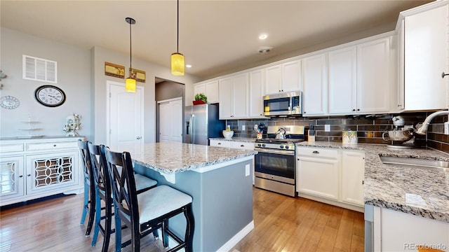 kitchen featuring sink, white cabinetry, appliances with stainless steel finishes, pendant lighting, and decorative backsplash