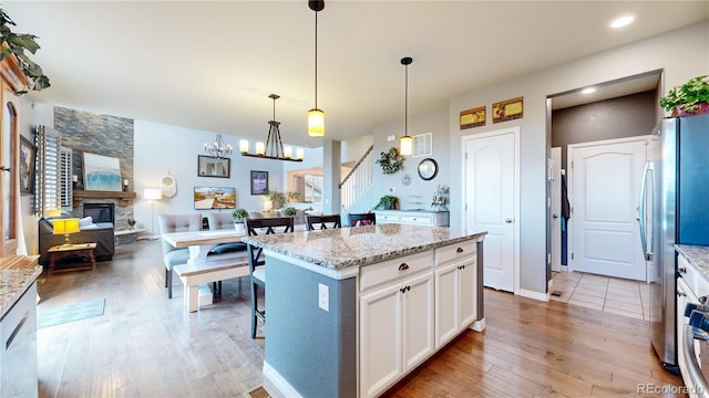 kitchen with a stone fireplace, white cabinetry, light stone counters, decorative light fixtures, and a kitchen island