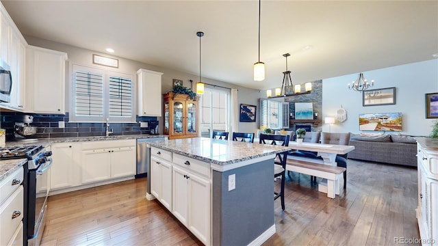 kitchen featuring white cabinetry, a center island, pendant lighting, stainless steel appliances, and light stone countertops