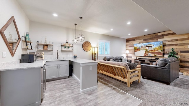 kitchen featuring sink, wood walls, light hardwood / wood-style flooring, kitchen peninsula, and pendant lighting