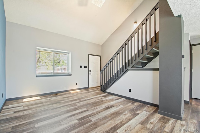 entryway with a skylight, light wood-type flooring, stairway, a high ceiling, and baseboards