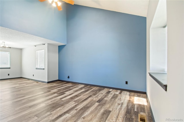 unfurnished living room with baseboards, vaulted ceiling, ceiling fan with notable chandelier, and wood finished floors