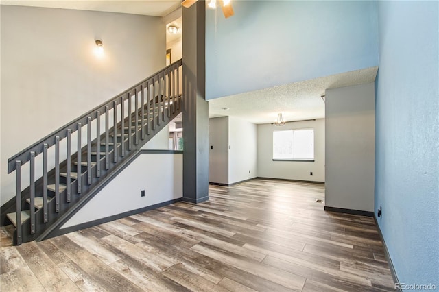 unfurnished living room featuring a ceiling fan, baseboards, a high ceiling, and wood finished floors