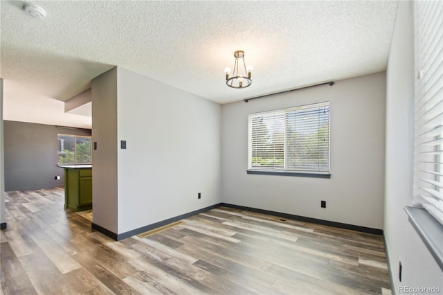 empty room with a textured ceiling, a chandelier, wood finished floors, and baseboards