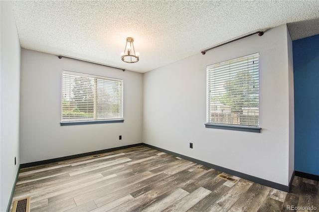 empty room featuring a textured ceiling, visible vents, and wood finished floors