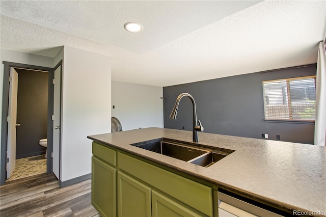 kitchen with a textured ceiling, dark wood finished floors, dishwasher, a sink, and green cabinetry