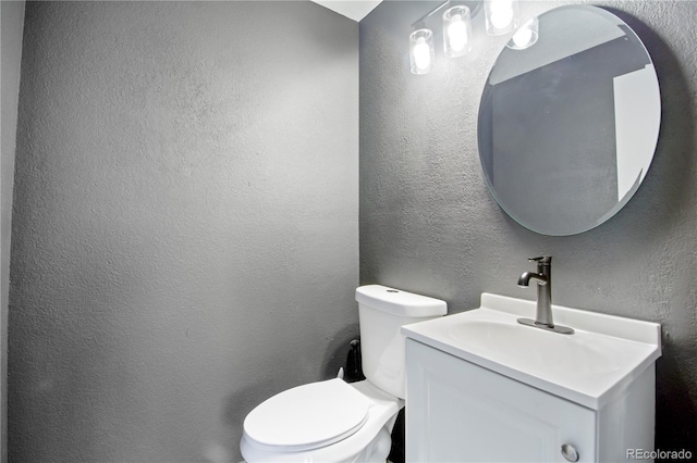 half bath with vanity, a textured wall, and toilet
