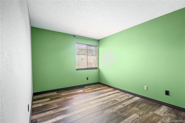 empty room with baseboards, a textured ceiling, a textured wall, and wood finished floors