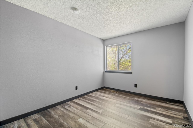 unfurnished room with baseboards, a textured ceiling, wood finished floors, and visible vents