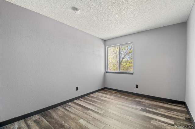 unfurnished room with baseboards, a textured ceiling, wood finished floors, and visible vents
