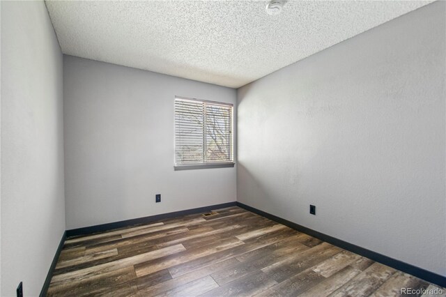 empty room with a textured ceiling, dark wood finished floors, and baseboards