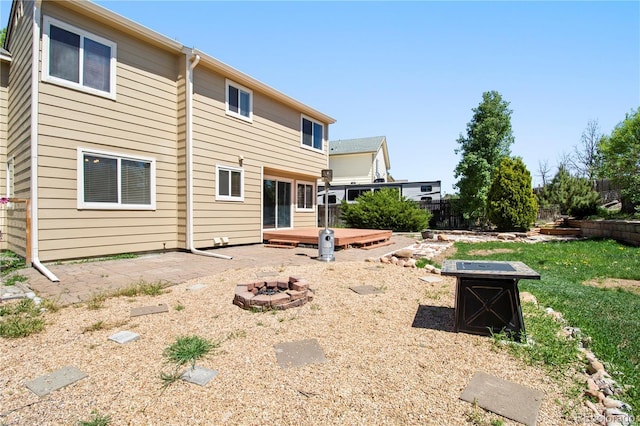 rear view of property featuring a fire pit, a patio area, a deck, and fence