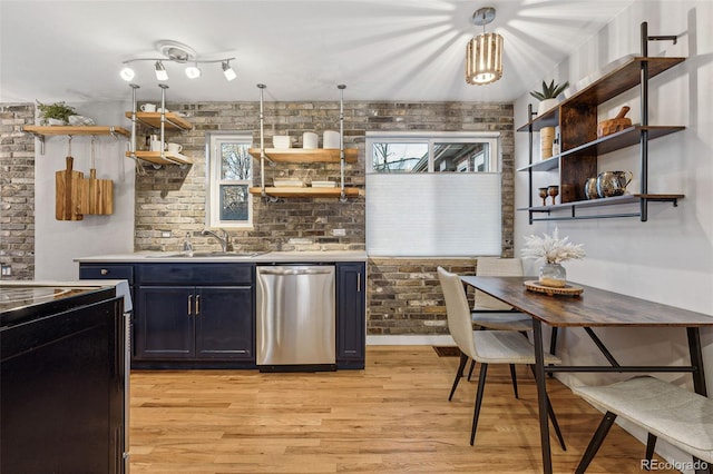 kitchen with stainless steel dishwasher, brick wall, sink, light hardwood / wood-style floors, and hanging light fixtures