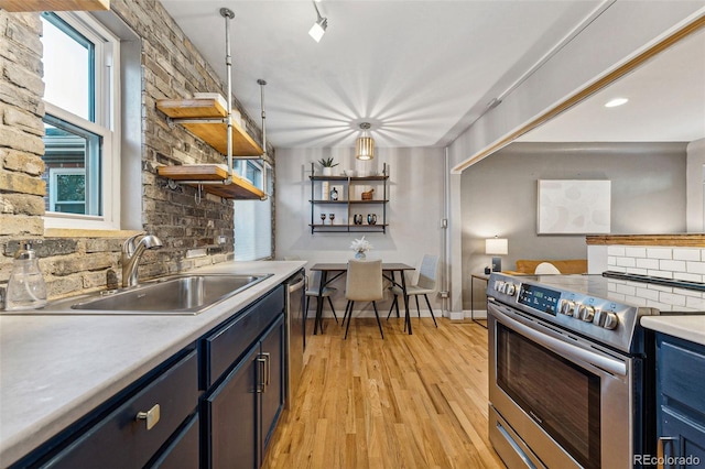 kitchen with stainless steel appliances, blue cabinets, sink, decorative light fixtures, and light hardwood / wood-style floors