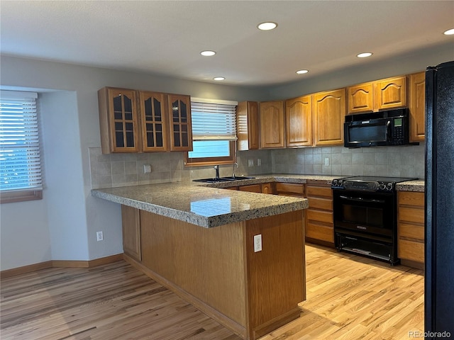 kitchen featuring sink, black appliances, decorative backsplash, kitchen peninsula, and light wood-type flooring