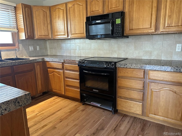 kitchen with tasteful backsplash, light hardwood / wood-style floors, sink, and black appliances