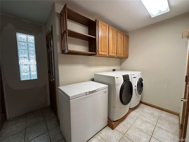 clothes washing area with washing machine and dryer, cabinets, and a textured ceiling