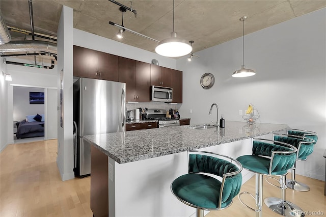 2229 Blake St Unit 505, Denver, CO 80205 - kitchen with stainless steel appliances, a sink, light wood-type flooring, dark brown cabinetry, and a peninsula