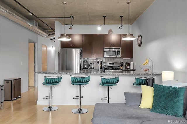2229 Blake St Unit 505, Denver, CO 80205 - kitchen with stainless steel appliances, decorative backsplash, dark brown cabinetry, a kitchen bar, and stone counters