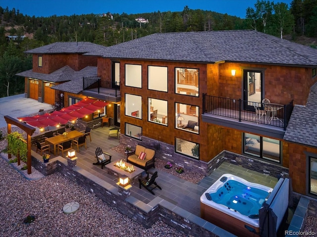 rear view of house featuring an outdoor hot tub, a fire pit, a patio, and a balcony